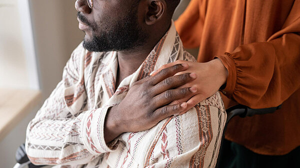 Two people touching hands, one person is seated